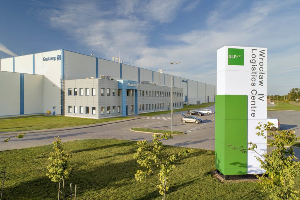 Front exterior of Wroclaw IV Logistics Centre where cars are parked up and a sign with GLP branding sits in the foreground.