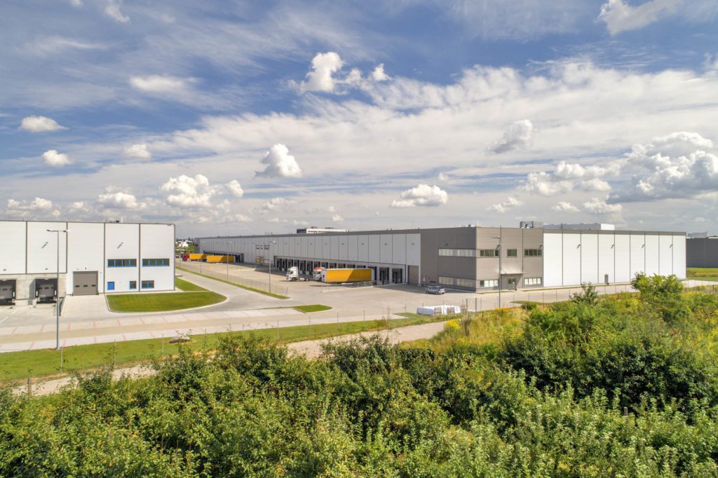 Wroclaw IV Logistics Centre from a distance, showing trees growing outside the perimeter and two large warehouses