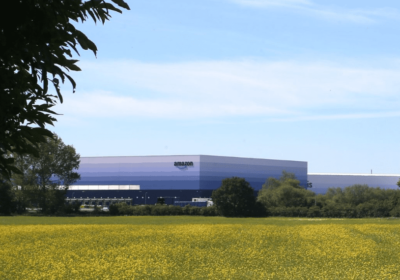 GLP Logistics Centre with Amazon branding on the outside is seen across a field of yellow flowers