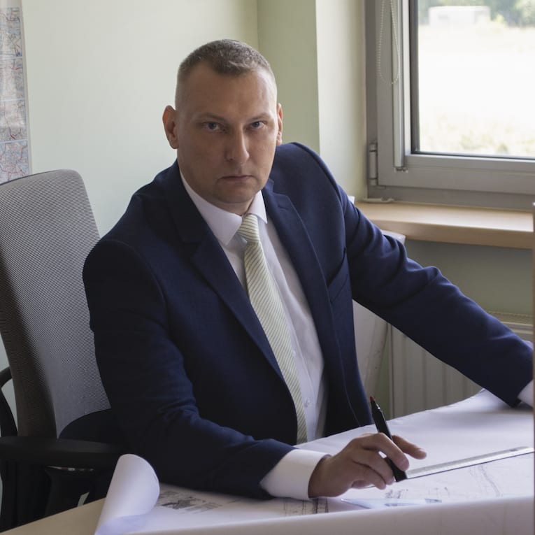 Artur sitting at a desk holding a pen and wearing a suit
