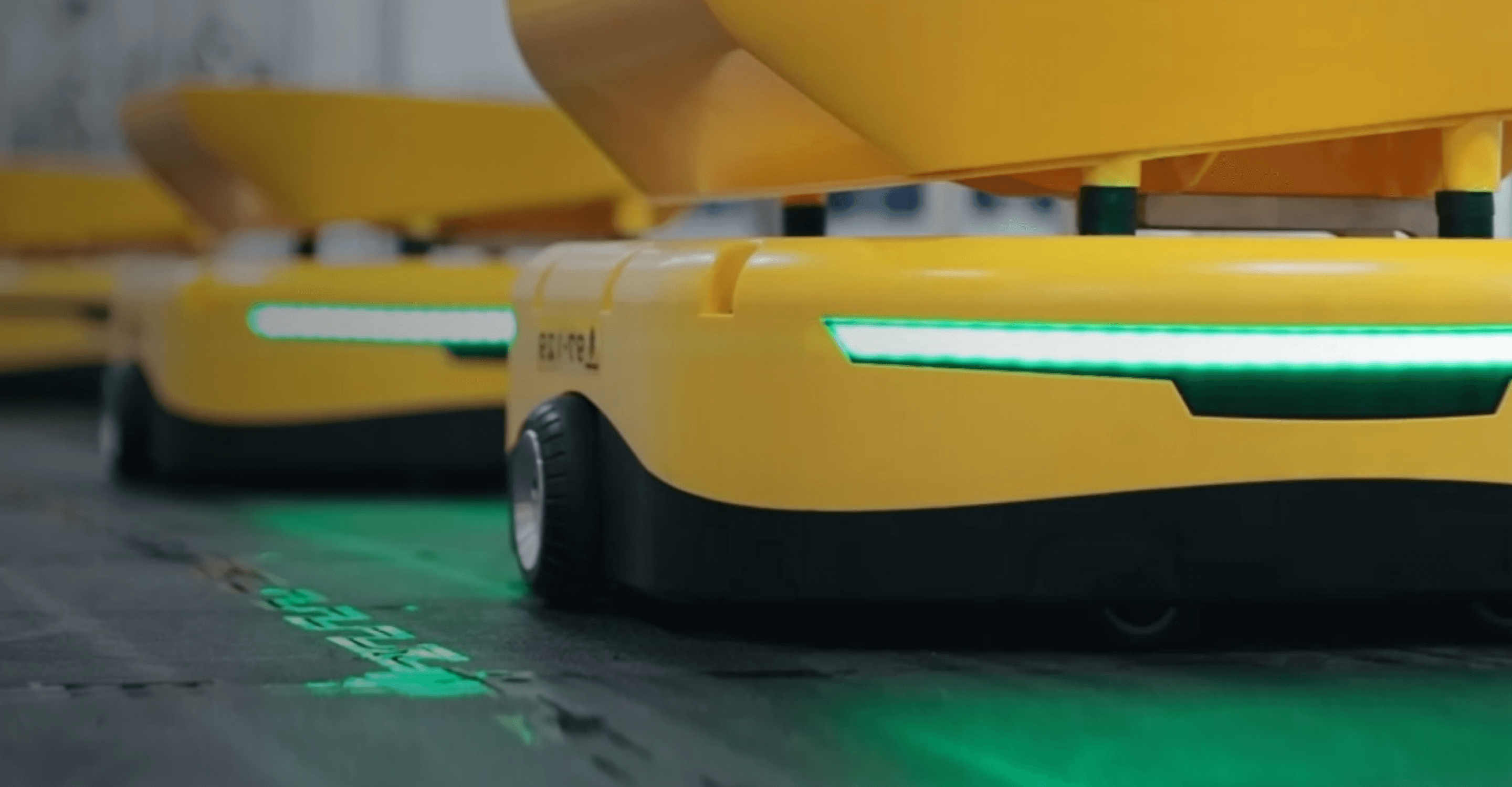 Close up of automated robots on wheels that have a green, glowing light on the front.