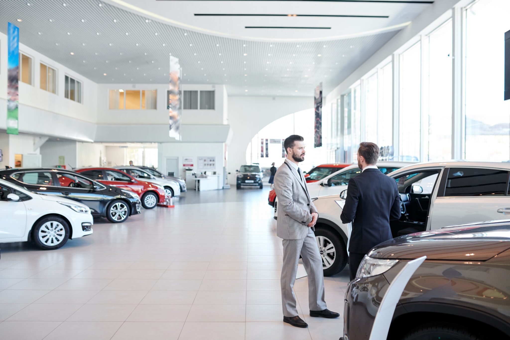 Two salesmen talking in a modern car showroom.